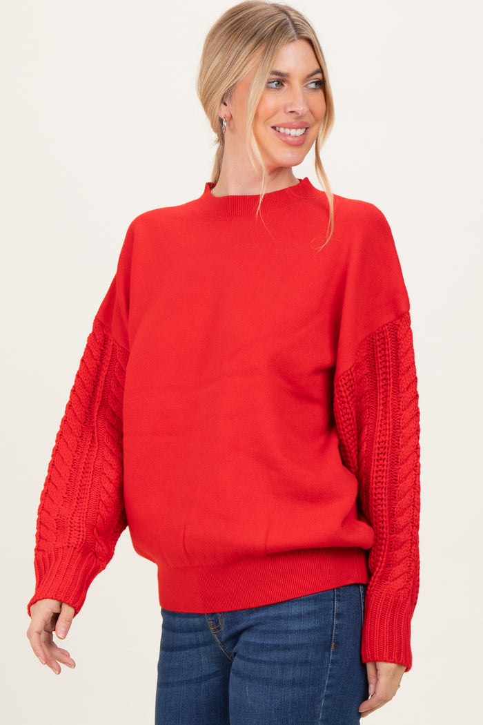 woman wearing a red oversized sweater with cable knit sleeves and a round neckline, smiling against a light background