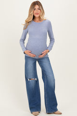 woman wearing a light blue long sleeve maternity top and distressed wide leg jeans, holding her baby bump