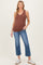 woman wearing a rust-colored sleeveless maternity tank top and blue cropped jeans, showing her baby bump