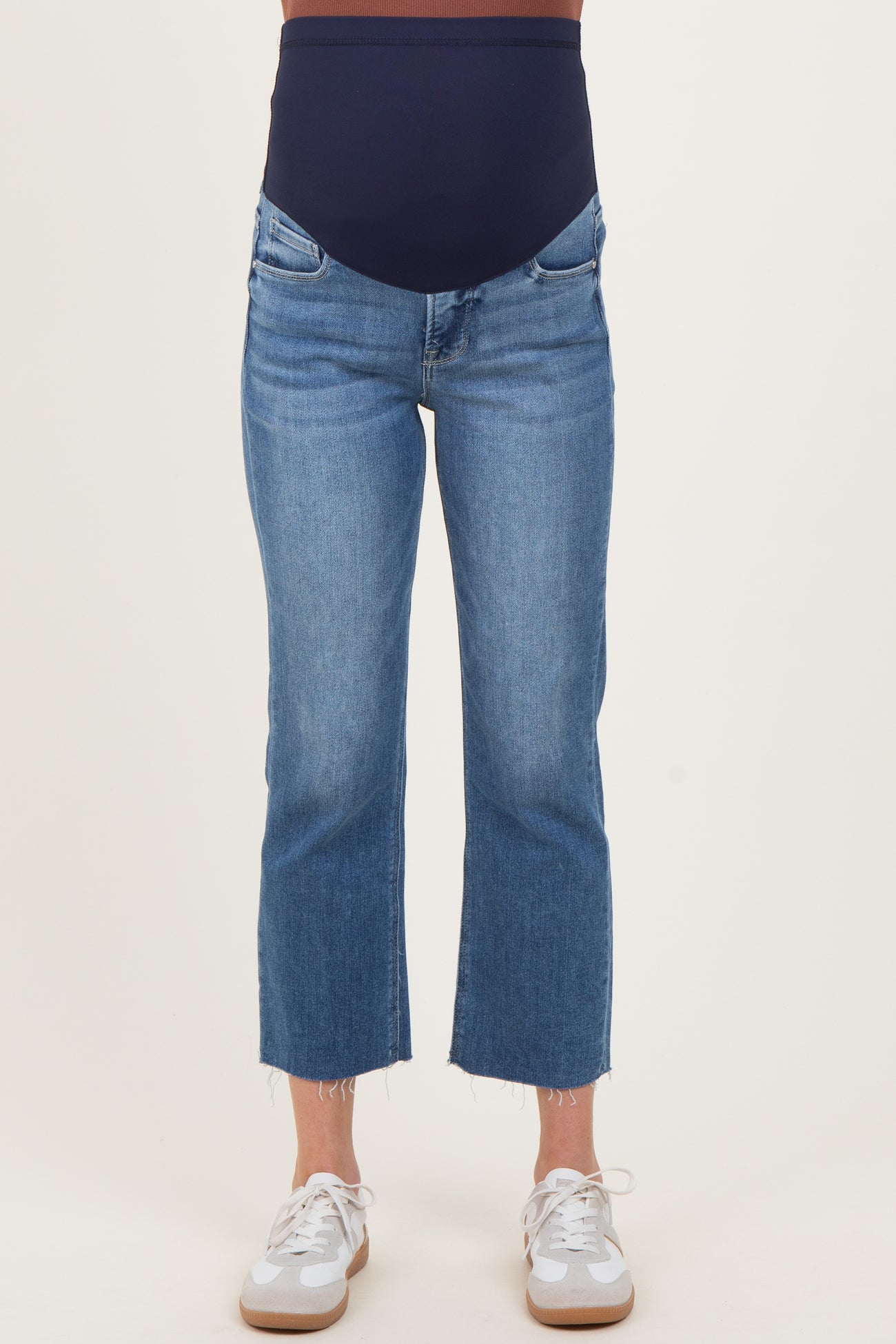 woman wearing a pair of light blue cropped maternity jeans with a navy over-the-bump panel and frayed hems