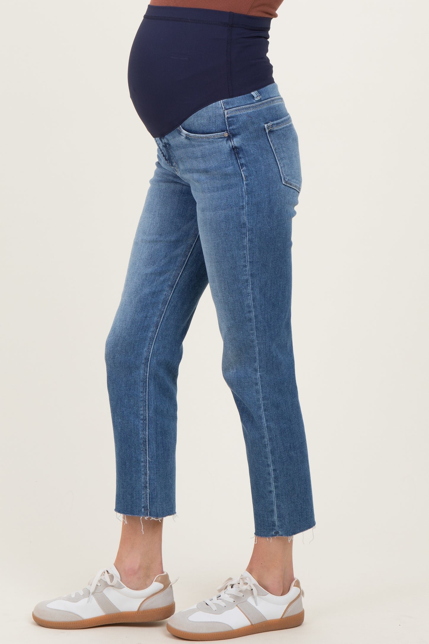woman wearing light blue maternity jeans with a fitted waistband, showcasing a visible baby bump and paired with white sneakers