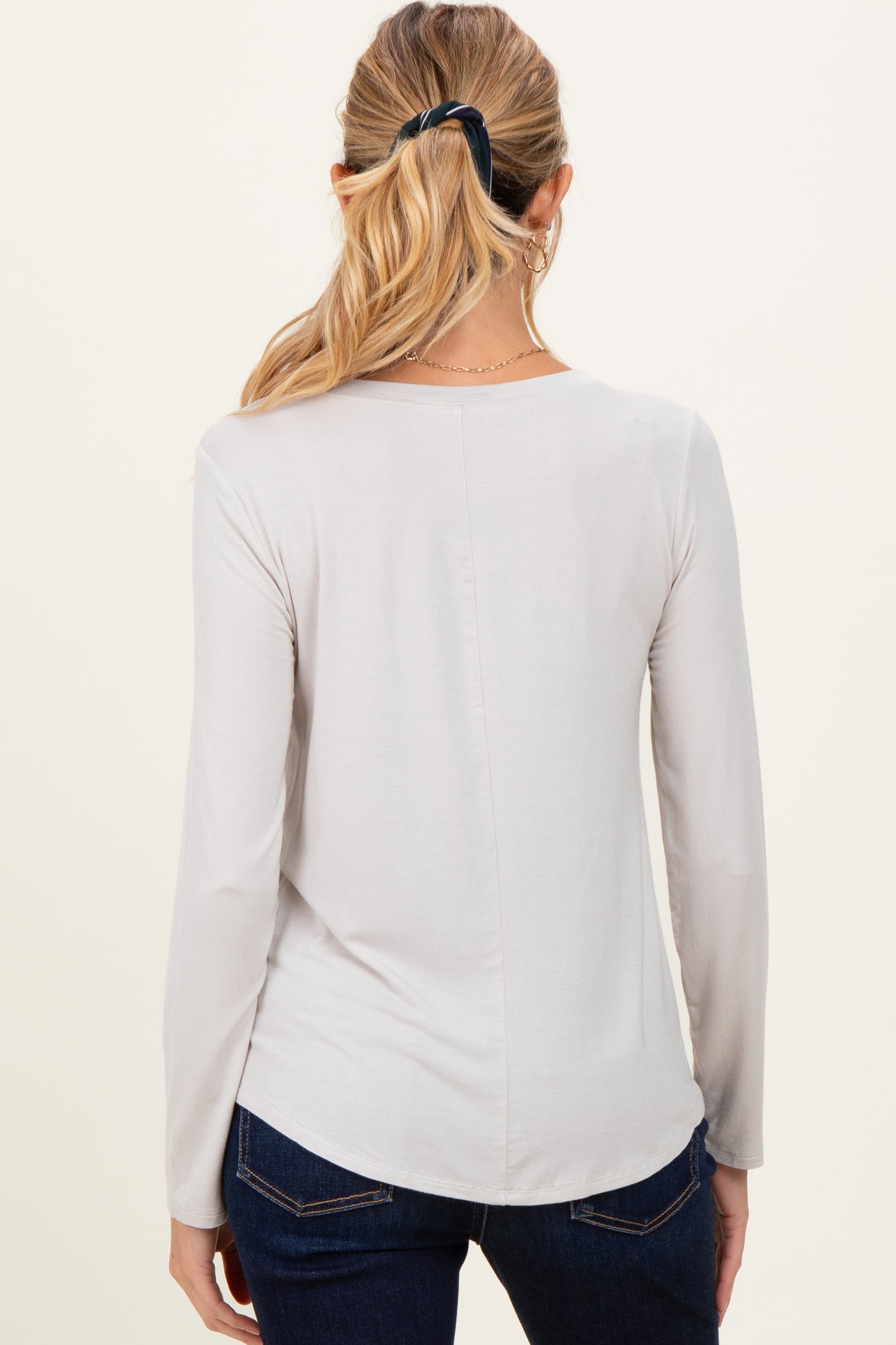 woman wearing a light grey long sleeve maternity top, viewed from the back, paired with dark jeans