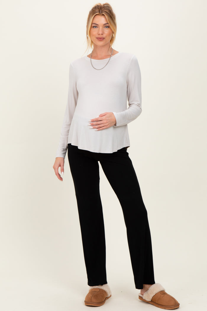 woman wearing a light gray maternity top with a flared hem and black maternity pants, holding her baby bump