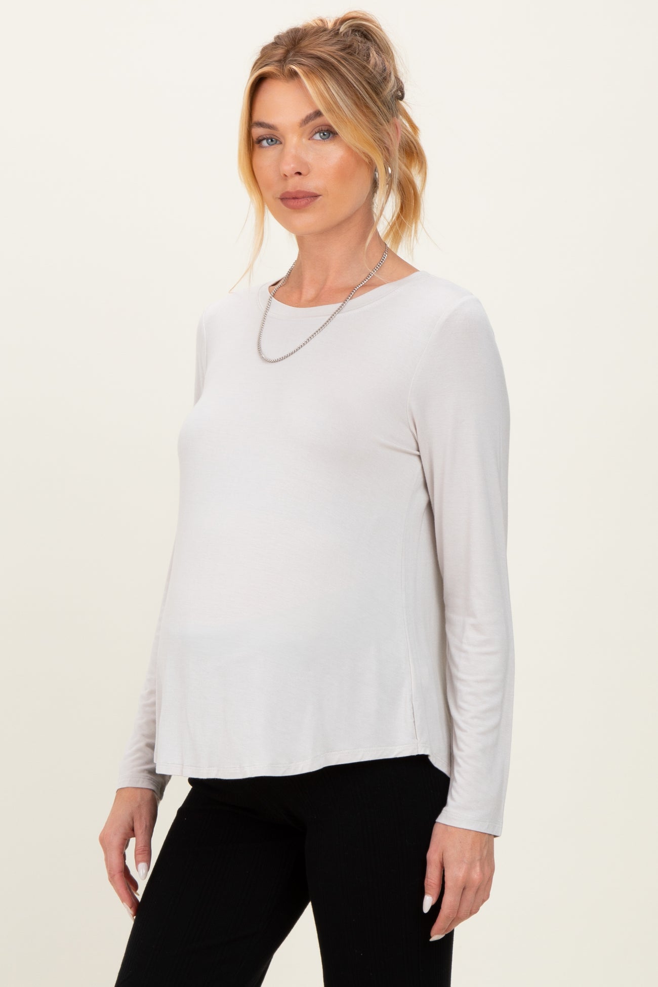 woman wearing a light beige long sleeve maternity top with a relaxed fit and a visible baby bump