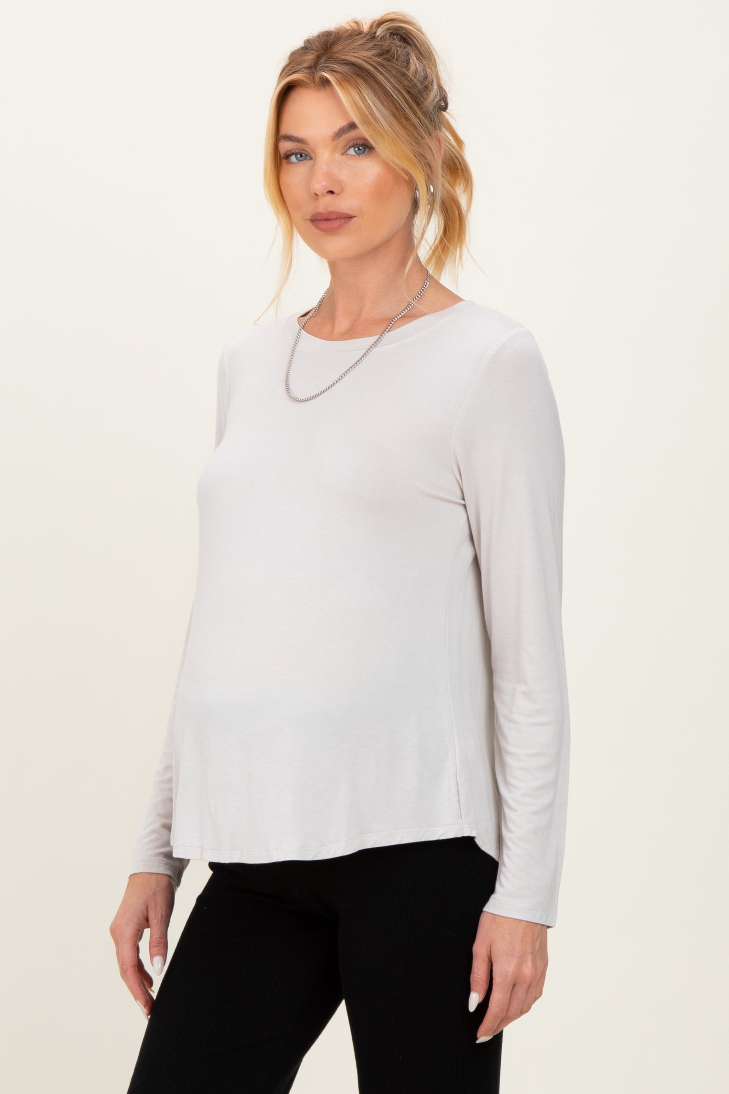 woman wearing a light beige long sleeve maternity top with a relaxed fit and a visible baby bump