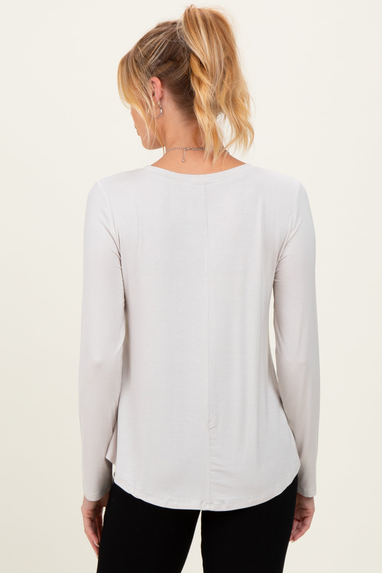 woman wearing a light gray long sleeve maternity top, viewed from the back with a slightly curved hem