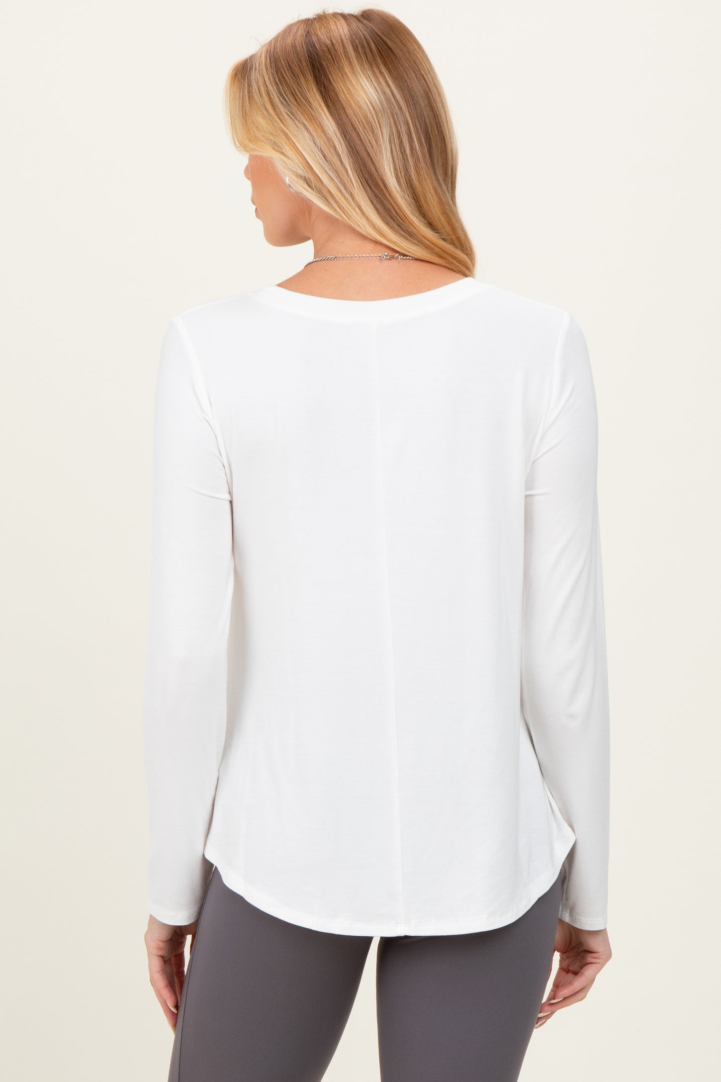 woman wearing a white long sleeve maternity top, shown from the back with a relaxed fit and curved hem