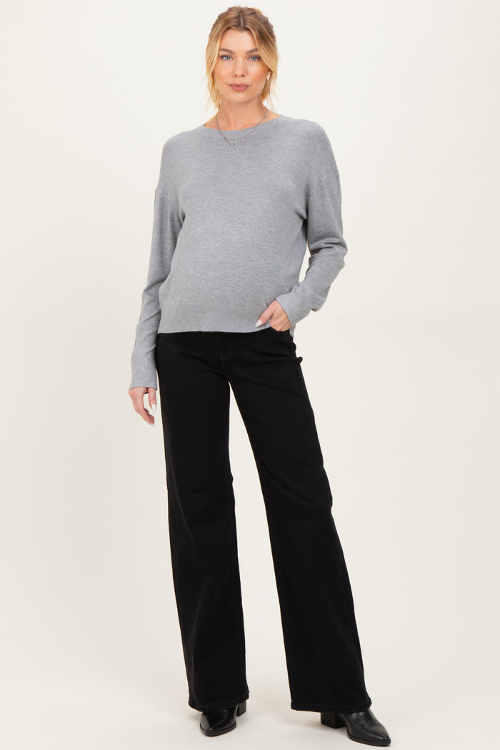 woman wearing a gray maternity sweater and black wide-leg pants, showcasing her baby bump