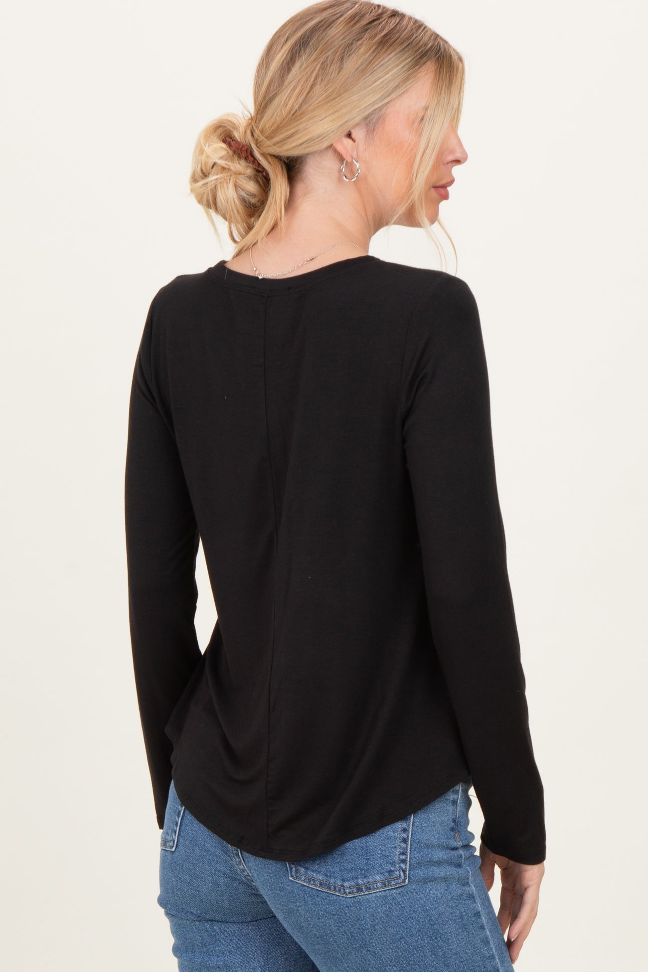 woman wearing a black long sleeve top with a rounded hem and back seam, paired with light blue jeans