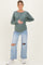 woman wearing a green long sleeve maternity top and distressed light blue jeans, holding her baby bump