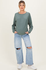 woman wearing a green long sleeve maternity top and distressed light blue jeans, displaying her baby bump