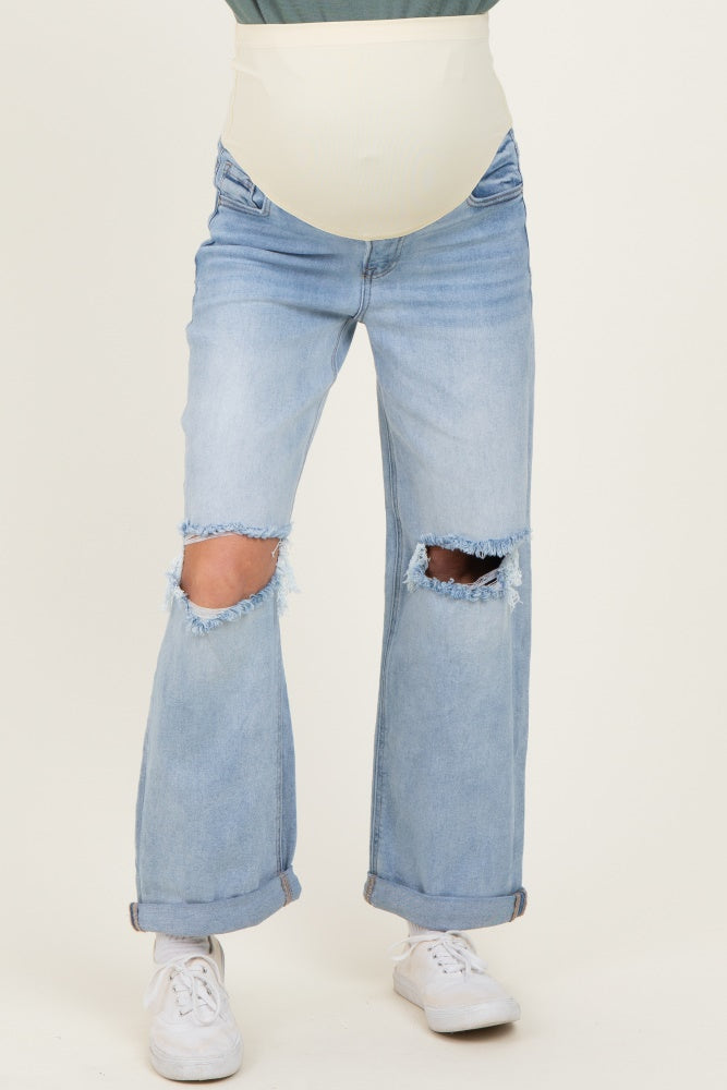 woman wearing light blue distressed maternity jeans with a cream-colored belly panel and rolled cuffs