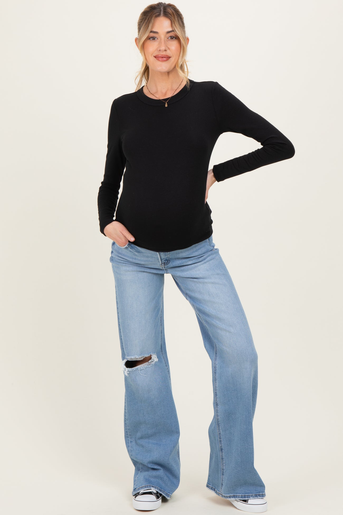 woman wearing a black long sleeve maternity top and distressed light blue maternity jeans, showing her baby bump
