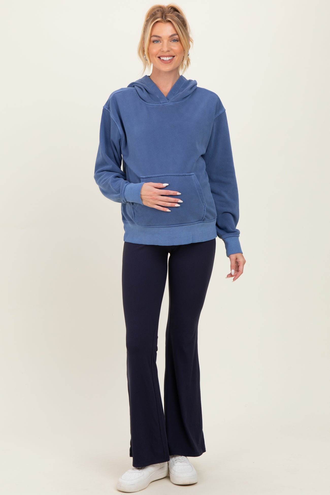 woman wearing a blue maternity hoodie and navy flared leggings, holding her baby bump