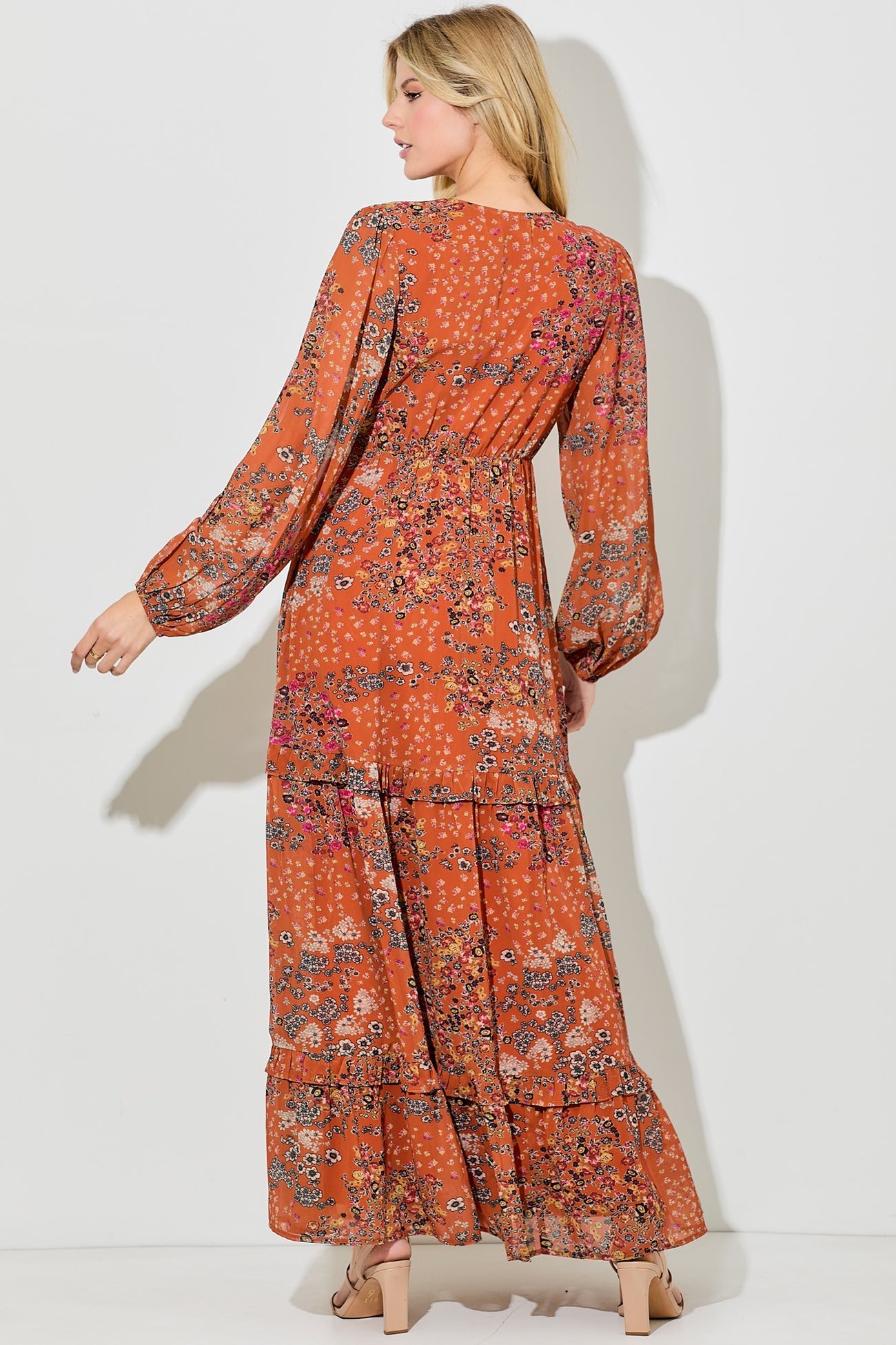 woman wearing an orange floral maxi dress with long sleeves and a tiered ruffle hem, viewed from the back