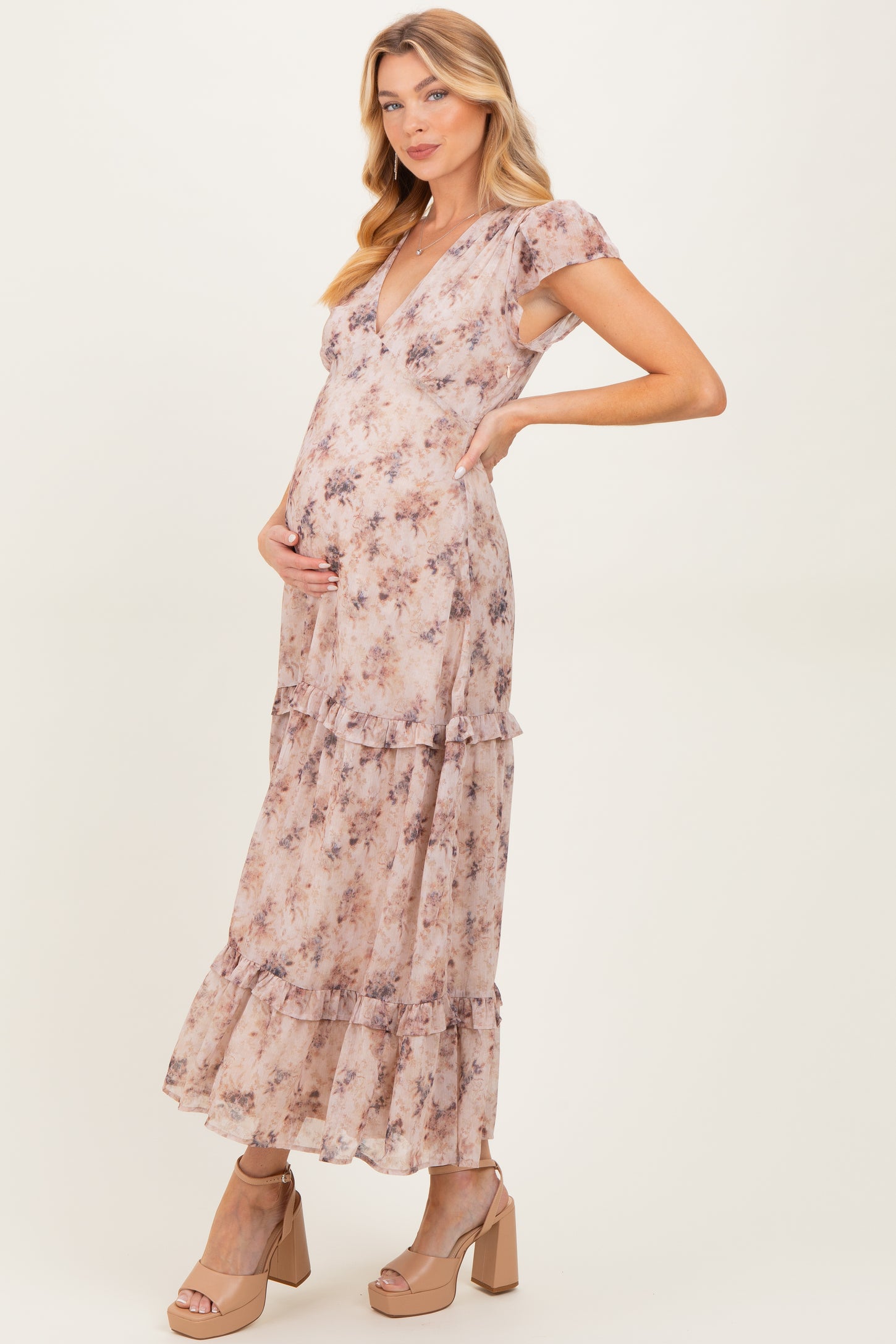 woman wearing a floral print maternity maxi dress with tiered ruffles and a v-neck, holding her baby bump