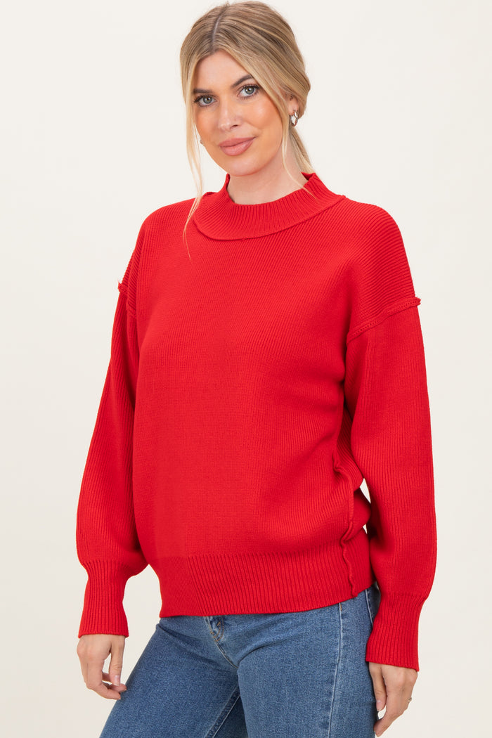 woman wearing a red oversized knit sweater with a high neckline and ribbed cuffs, paired with blue jeans