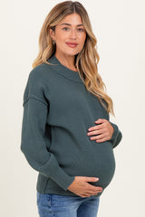 woman wearing a dark green oversized maternity sweater and holding her baby bump