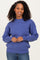 woman wearing a purple oversized knit sweater and blue jeans, smiling at the camera