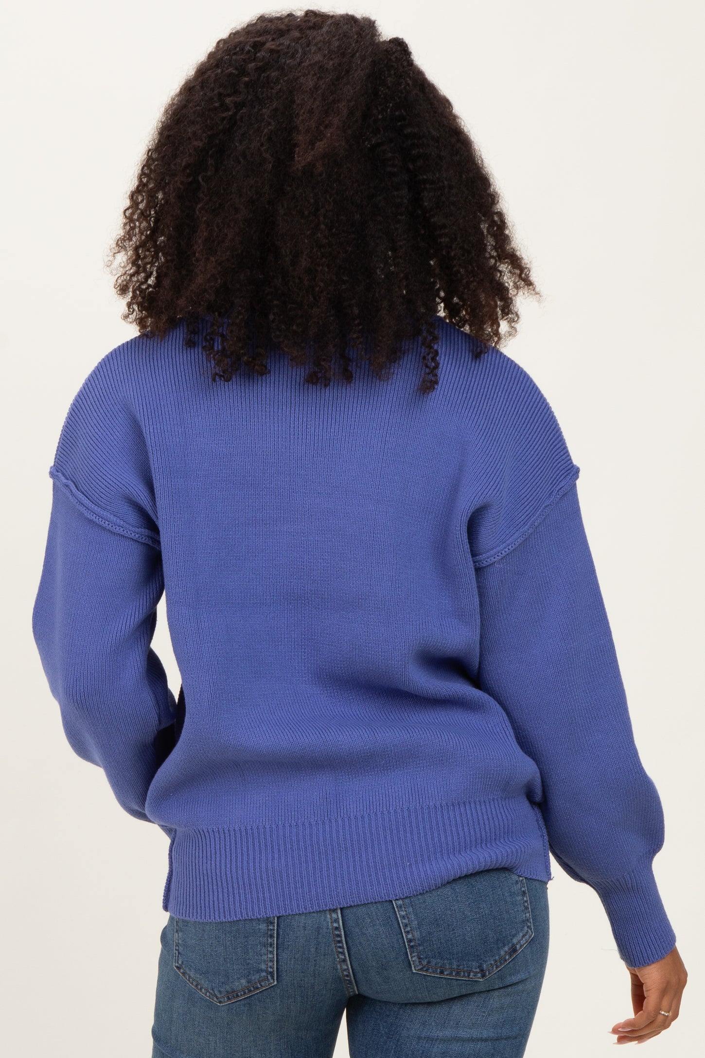 woman wearing a blue oversized sweater with ribbed detailing, viewed from the back, paired with denim jeans