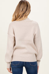 woman wearing a light beige oversized maternity sweater with ribbed texture and balloon sleeves, seen from the back