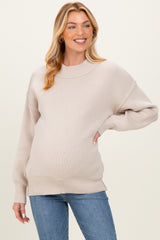 woman wearing a light beige oversized maternity sweater and showing her baby bump with blue jeans