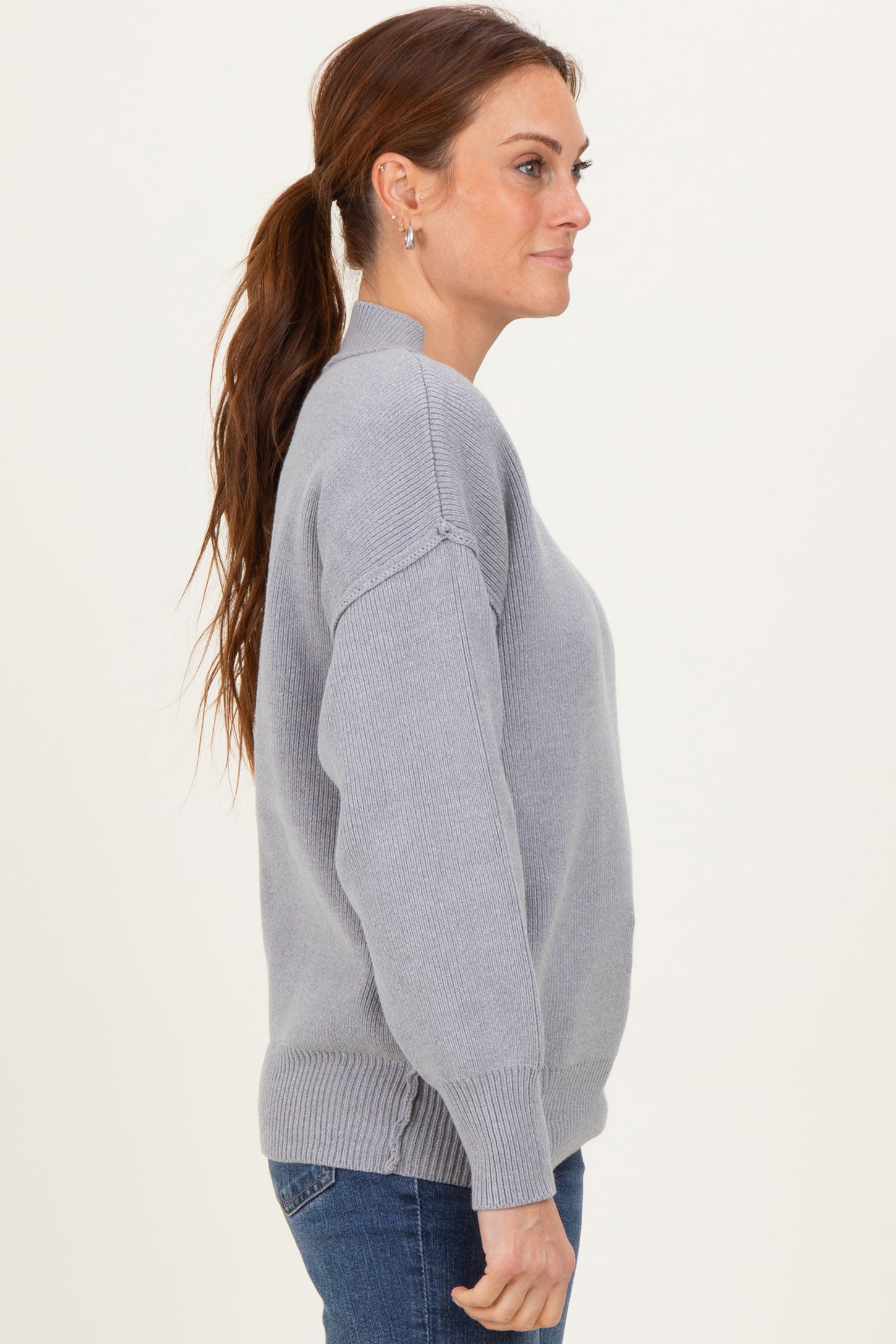 woman wearing a light gray oversized sweater with a mock neck and dropped shoulders paired with blue jeans