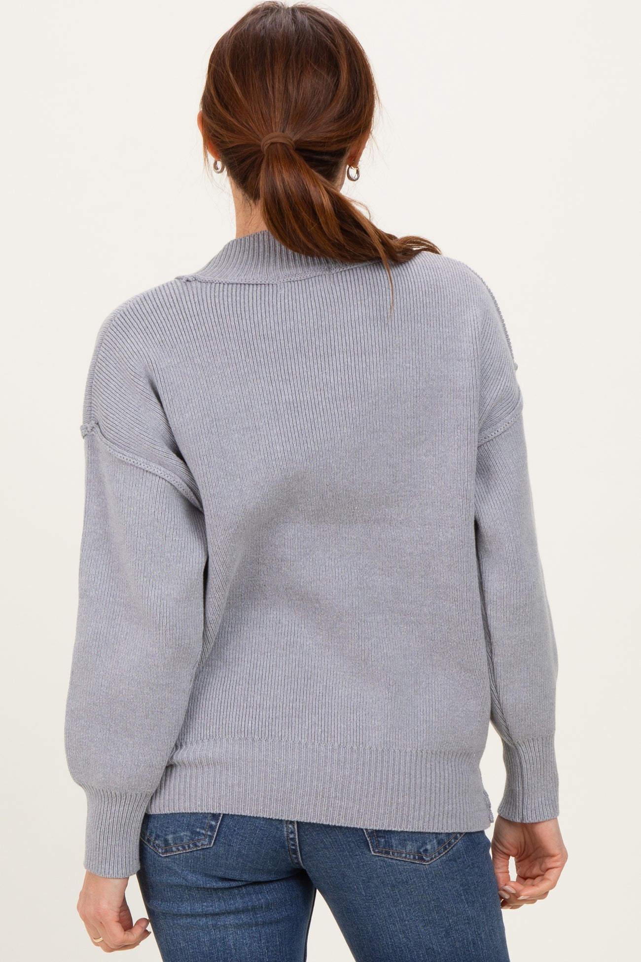 woman wearing a cozy light gray loose-fit sweater with a ribbed texture, seen from the back