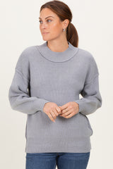 woman wearing a light gray oversized sweater with ribbed texture and a boat neckline, styled with blue jeans