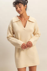 woman wearing a cream-colored sweater dress with a wide collar and long sleeves, smiling softly
