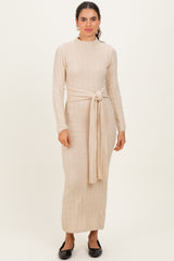 woman wearing a light beige long sleeve knit dress with a tied waist and a straight fit, standing against a neutral background
