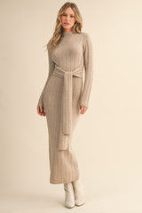 woman wearing a beige long sleeve ribbed knit maxi dress with a tie waist and styled with white ankle boots