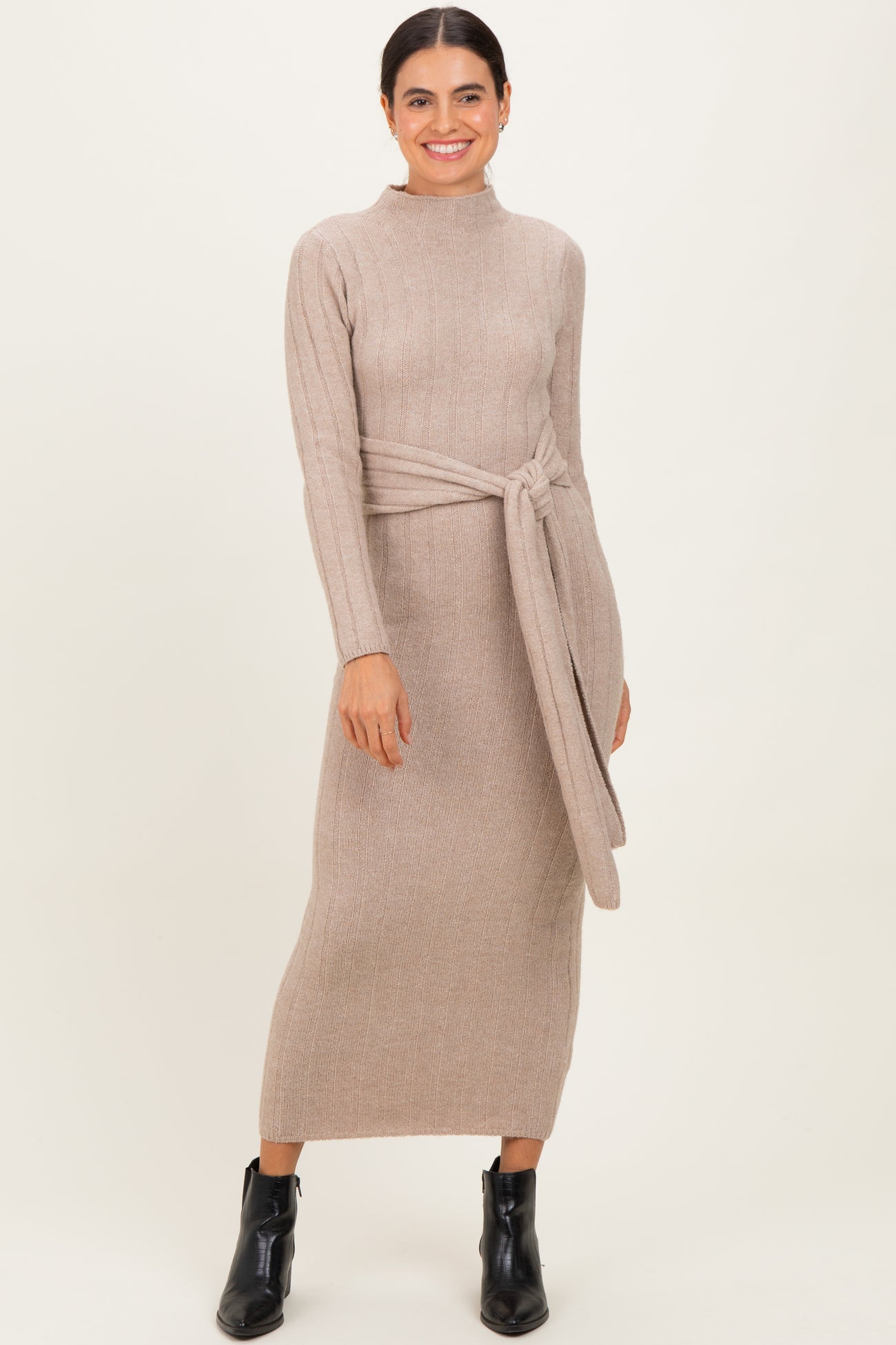woman wearing a taupe ribbed knit long sleeve dress with a tied waist and ankle boots