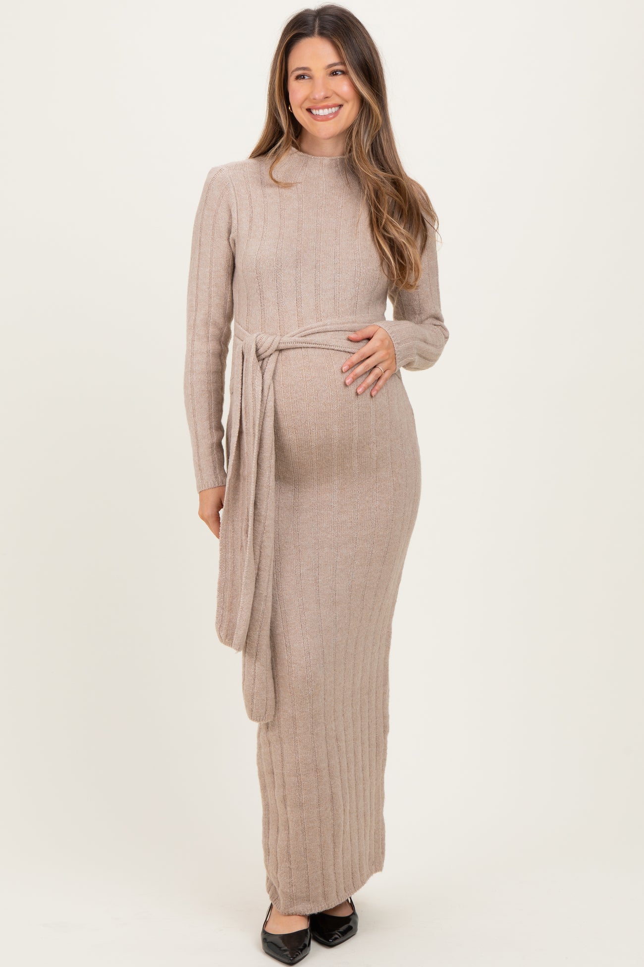 woman wearing a beige ribbed long sleeve maternity dress with a tie waist and visible baby bump