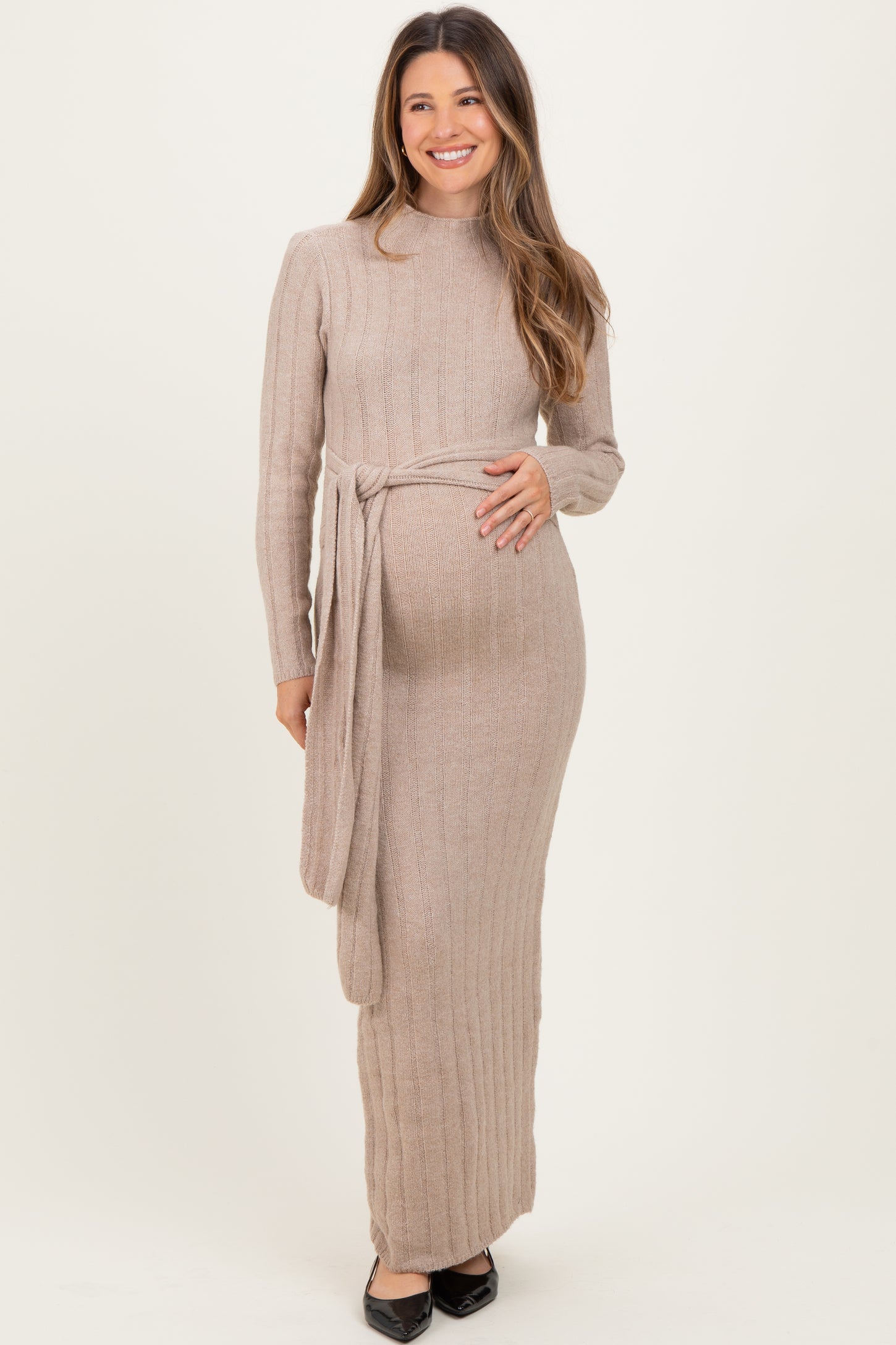 woman wearing a beige ribbed long sleeve maternity dress with a tie waist and visible baby bump