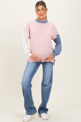 woman wearing a striped color-block maternity sweater in pink and blue with a visible baby bump and blue jeans