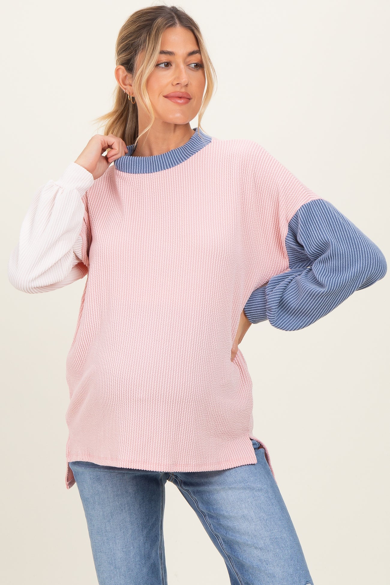 woman wearing a pink and blue color-blocked maternity sweater with ribbed texture and balloon sleeves, showing baby bump