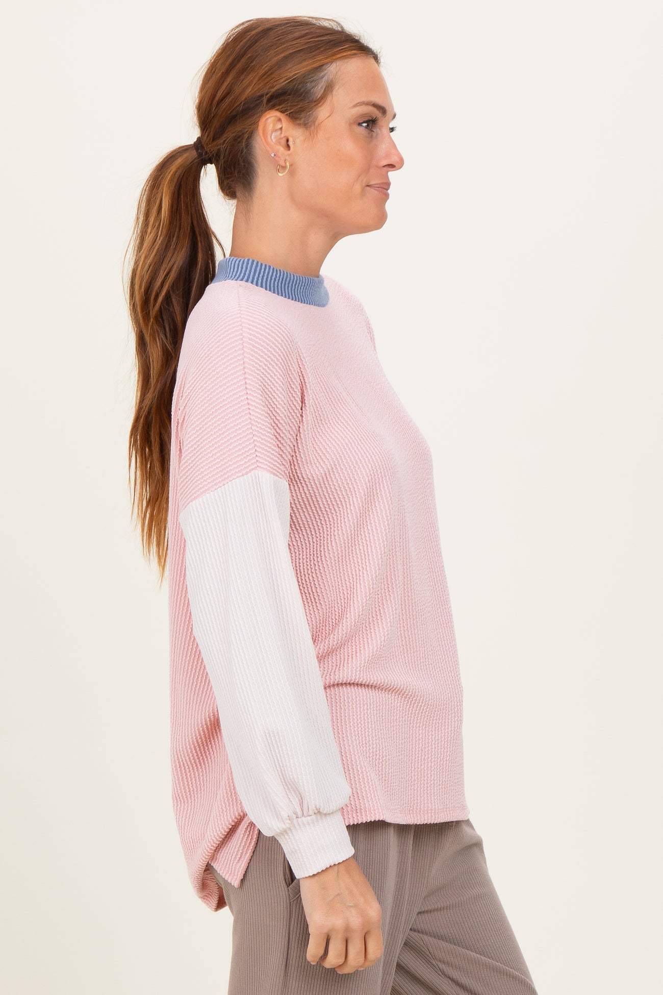 woman wearing a light pink ribbed long sleeve top with blue neckline and white sleeves, styled casually