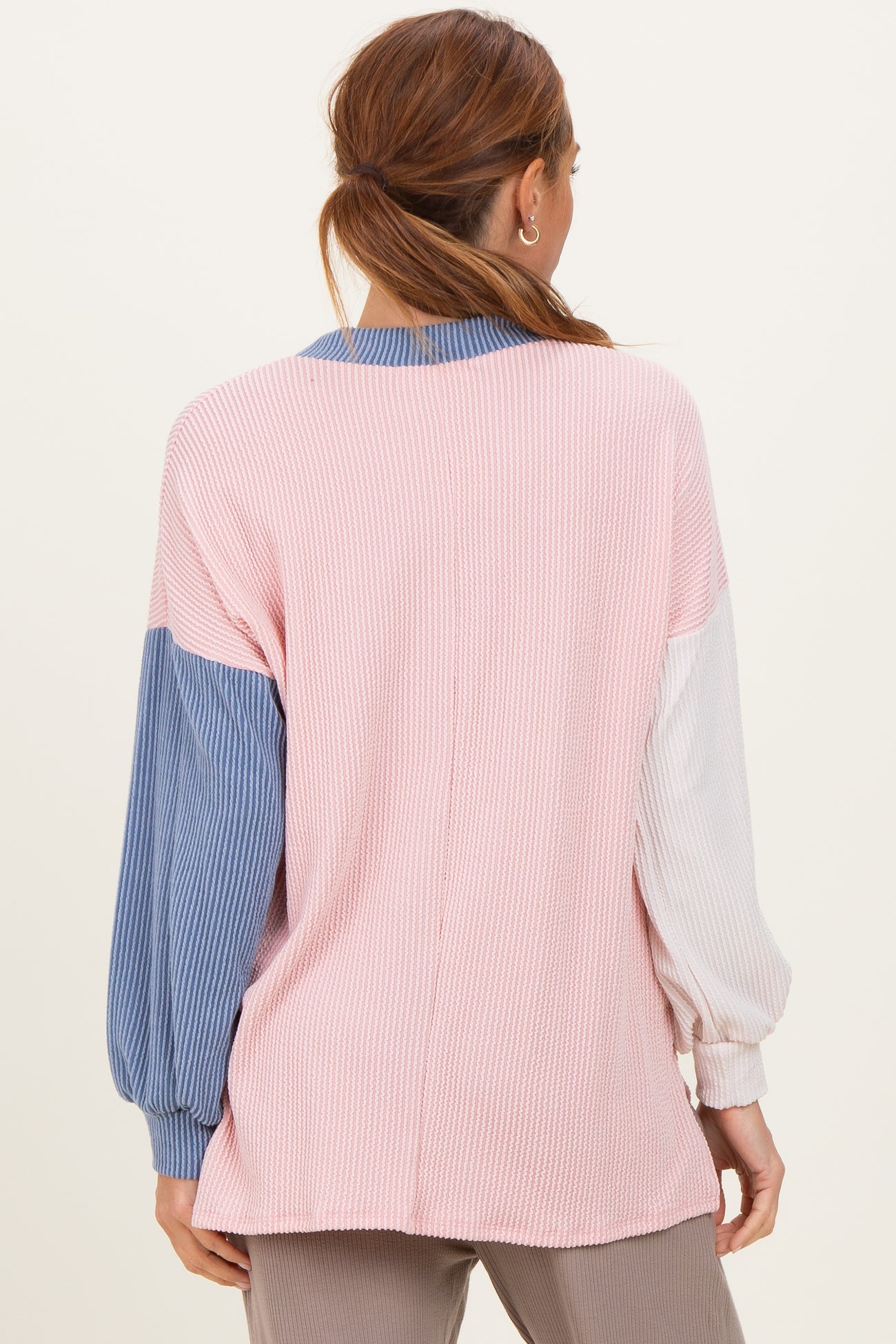 woman wearing a color-block long sleeve top in pink, blue, and white with a loose fit and ribbed texture from the back
