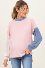woman wearing a color-blocked pink and blue maternity top with ribbed texture and long sleeves, gently cradling her baby bump