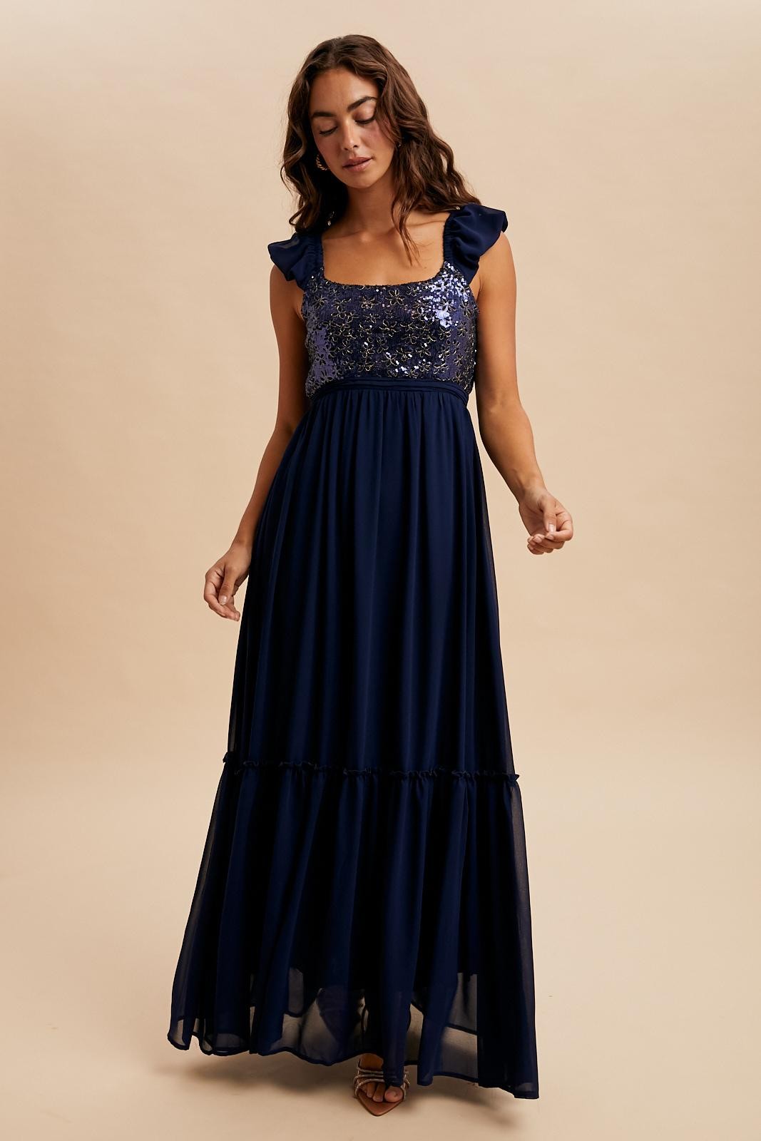 woman wearing a navy blue maxi dress with sequined bodice and ruffled sleeves