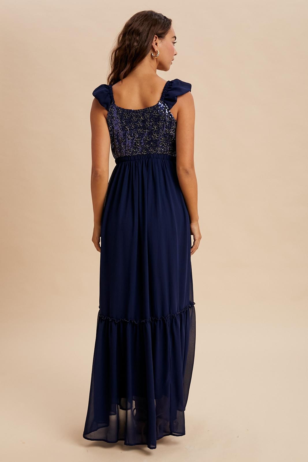 woman wearing a navy blue maxi dress with ruffled sleeves and a tiered skirt, shown from the back