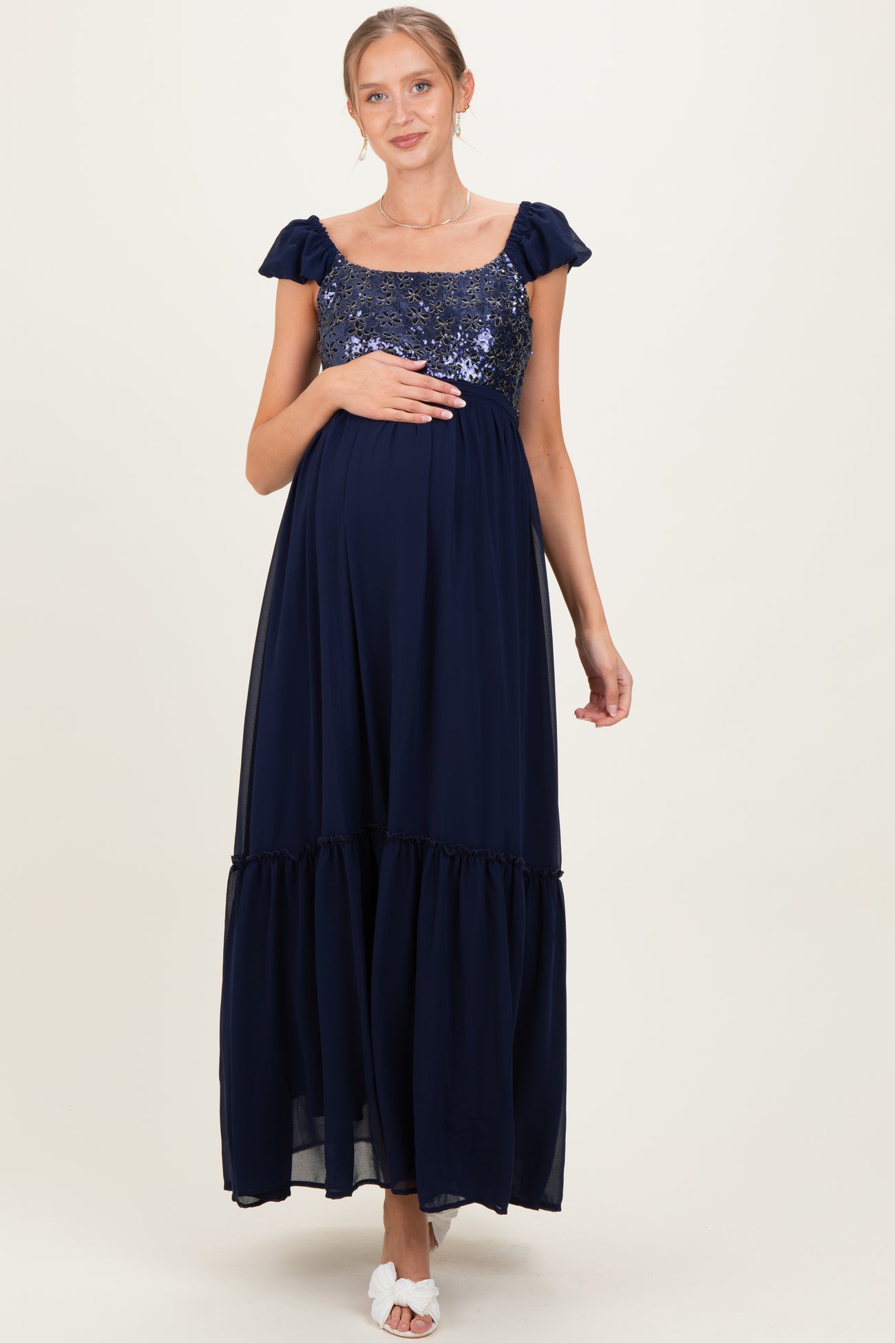 woman wearing a navy blue maternity maxi dress with sequin details and ruffled hem, showing her baby bump