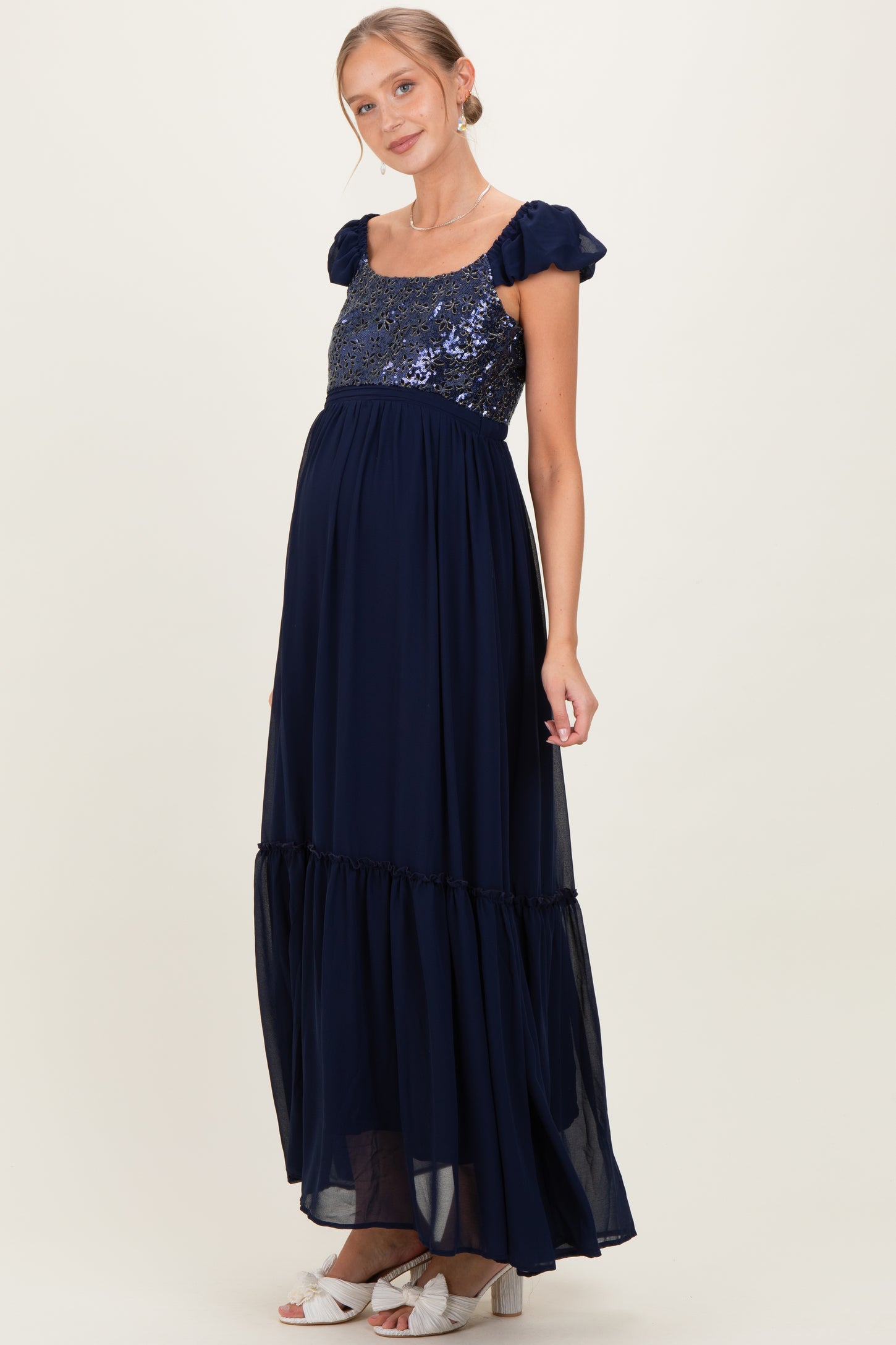 woman wearing a navy blue maternity dress with sequin bodice and flowy skirt, showing her baby bump