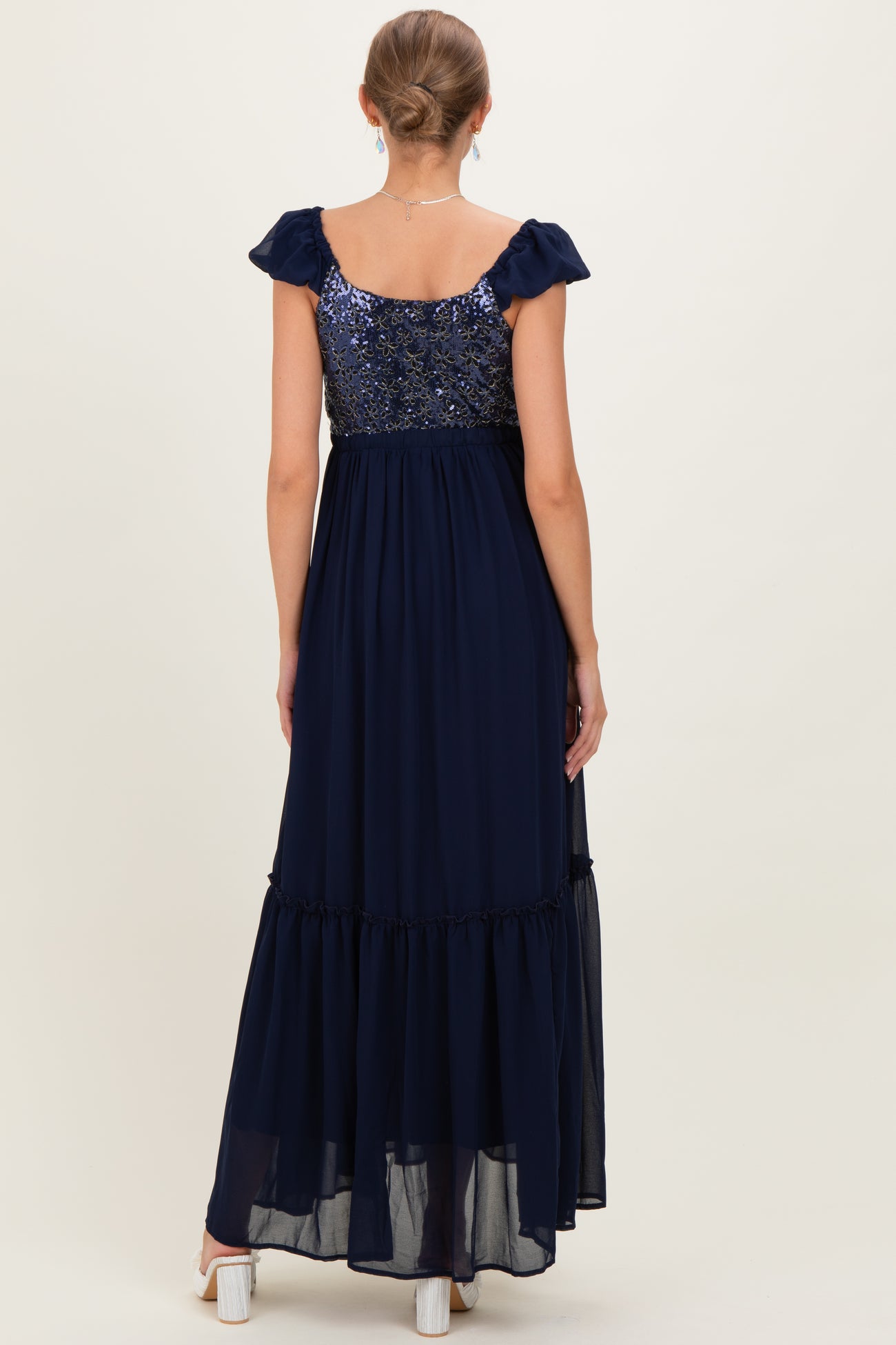 woman wearing a navy blue maternity maxi dress with a sequined bodice and flutter sleeves, showing the back view