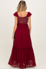 woman wearing a burgundy maternity maxi dress with flutter sleeves and a gathered waist, showing the back view