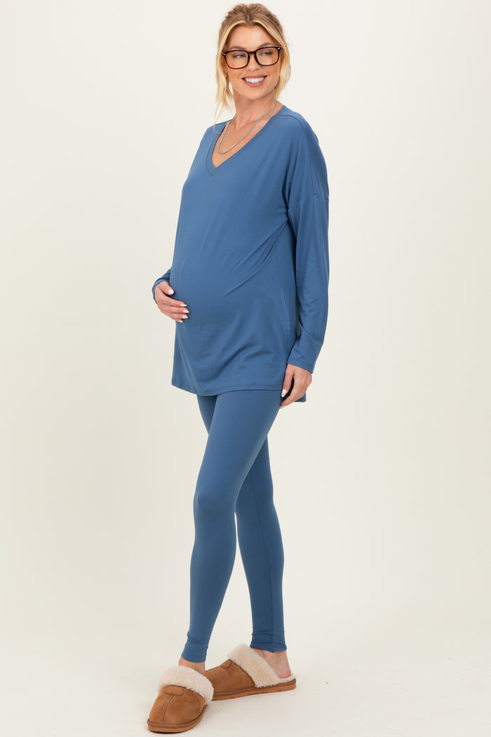 woman wearing a blue maternity tunic and matching leggings, holding her baby bump with a smile