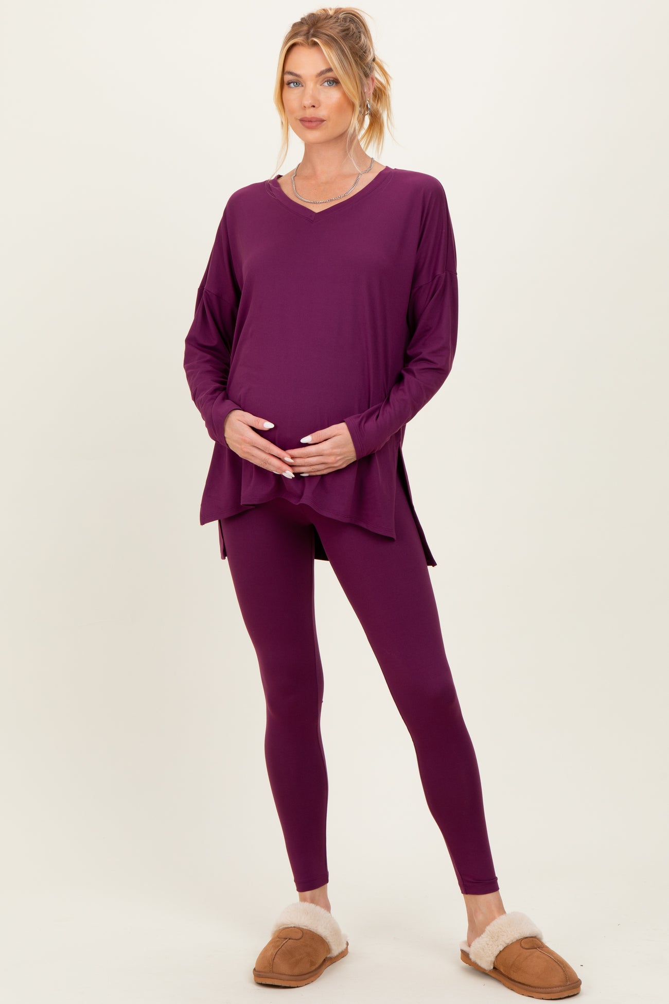woman wearing a purple maternity top and matching leggings, holding her baby bump