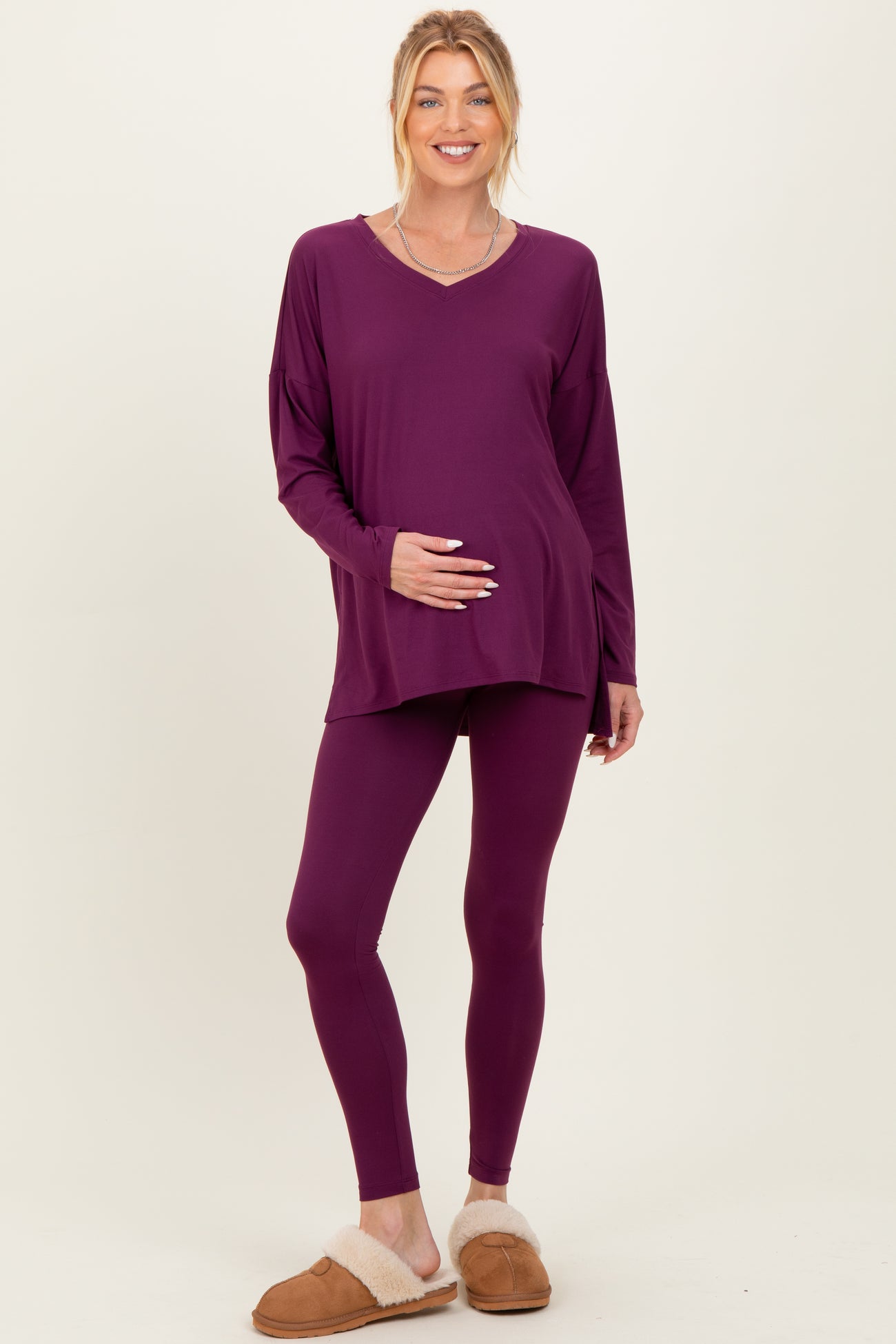 woman wearing a purple maternity top and matching leggings, holding her baby bump