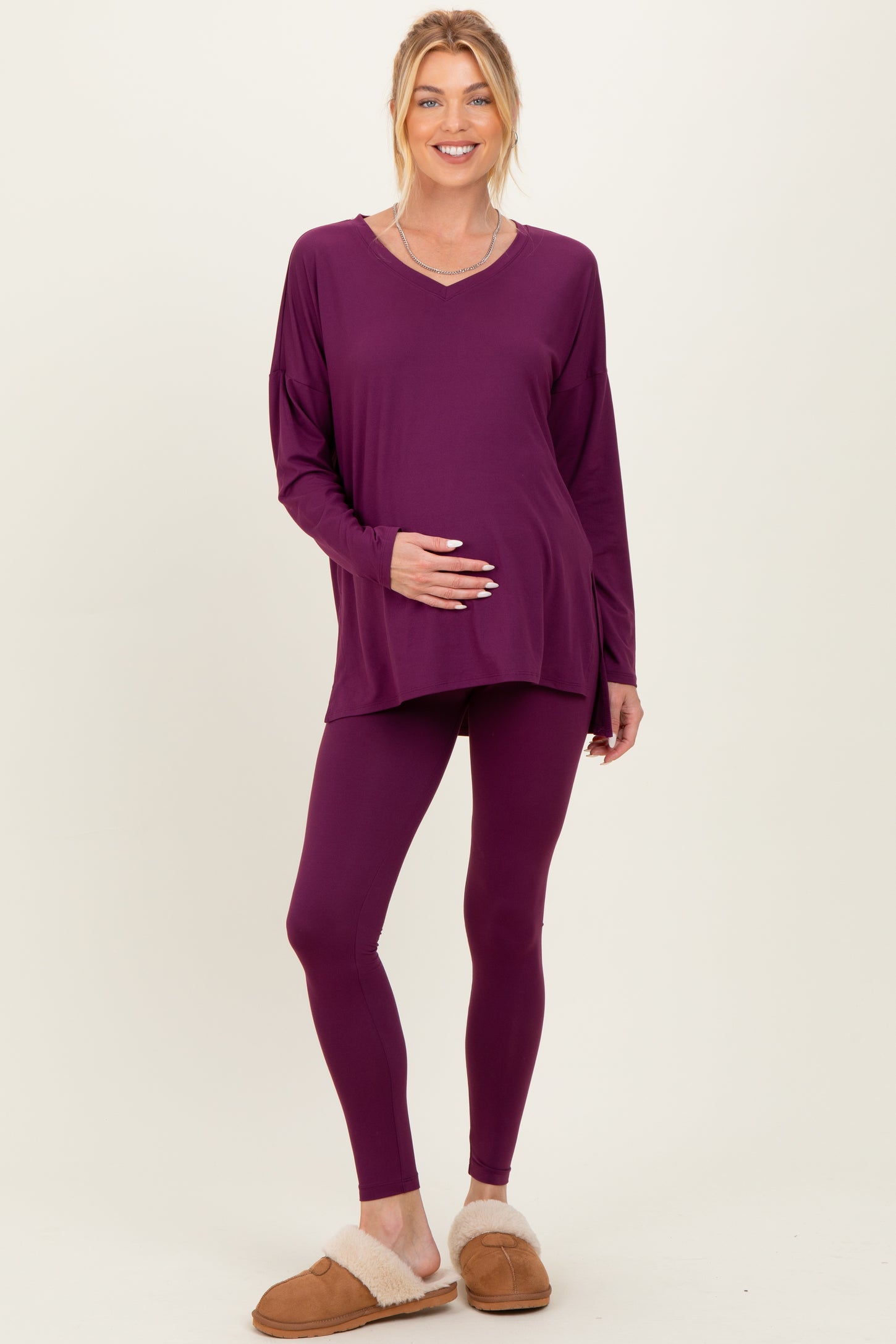 woman wearing a purple maternity top and matching leggings, holding her baby bump
